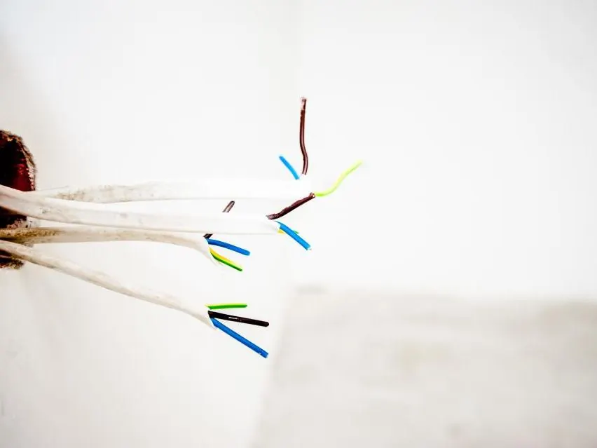 Cables eléctricos pelados saliendo de una pared blanca recién preparada