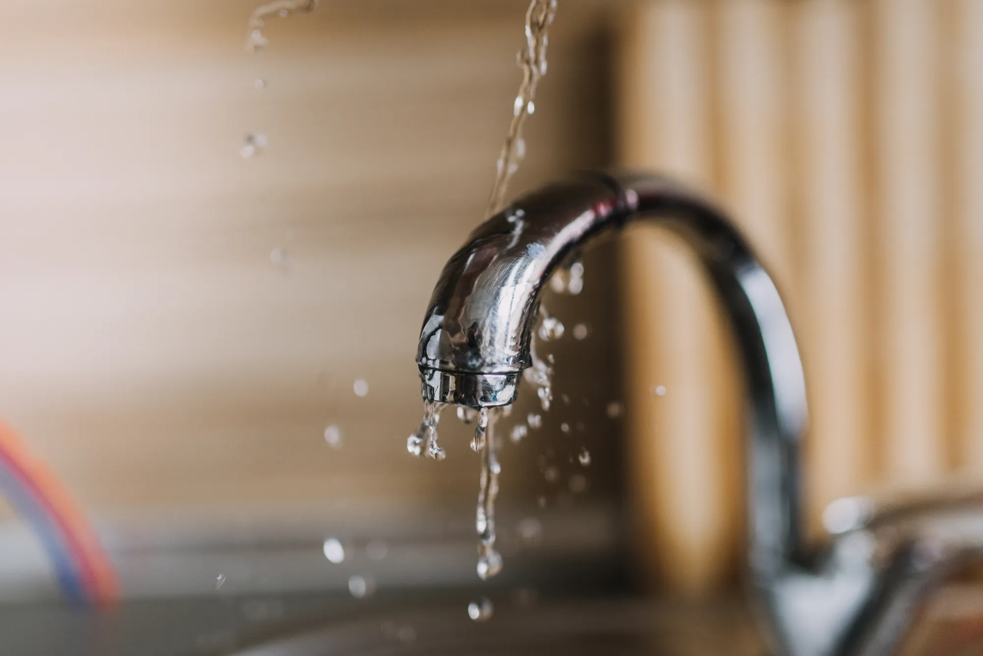 Gotas de agua caen de un grifo cromado de cocina con fondo de madera desenfocado