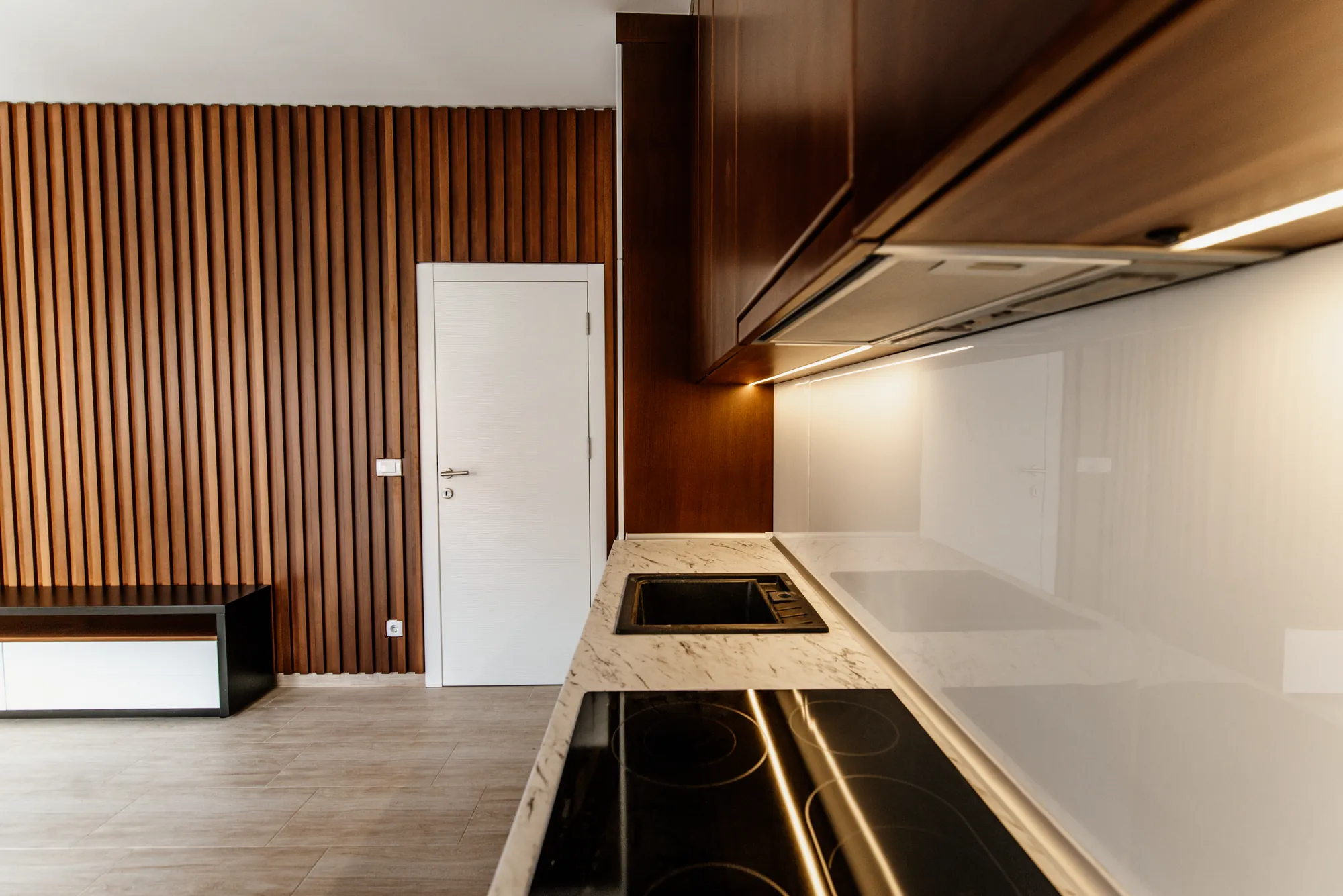 Cocina abierta con luz bajo los muebles altos, encimera de madera y placa negra