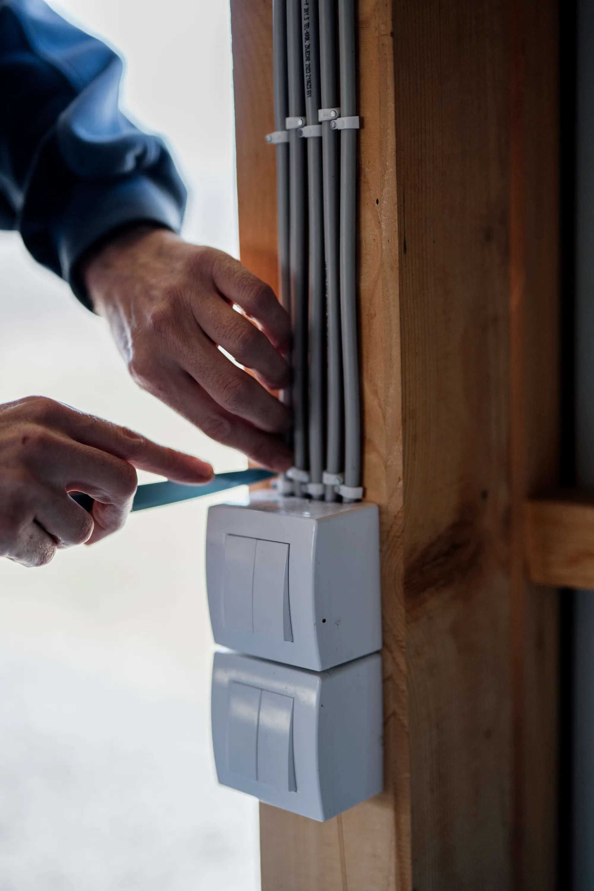 Manos con destornillador ajustan una caja de interruptores bajo varios tubos de cableado gris