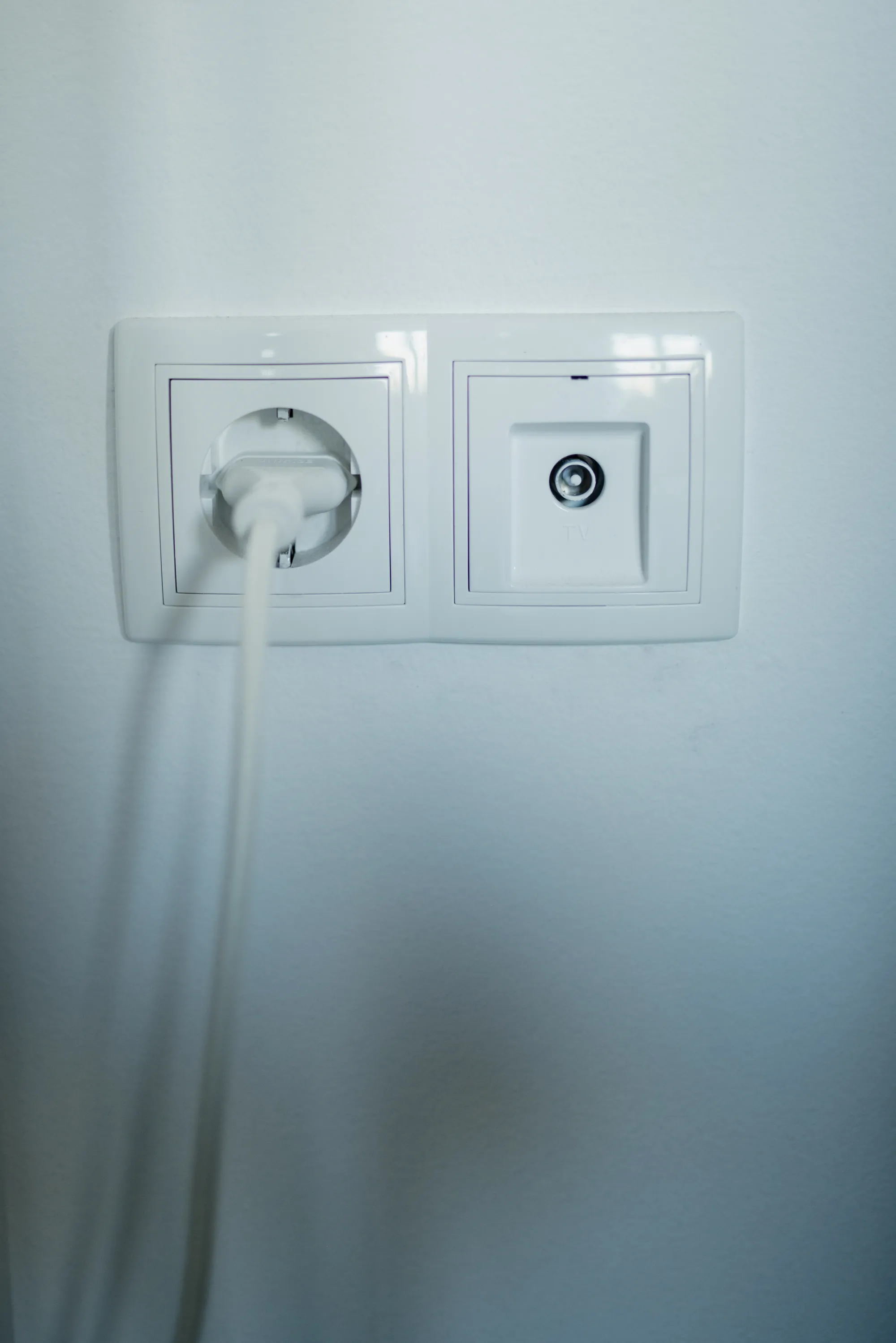 Enchufe blanco con la clavija conectada junto a una toma de antena en una pared clara