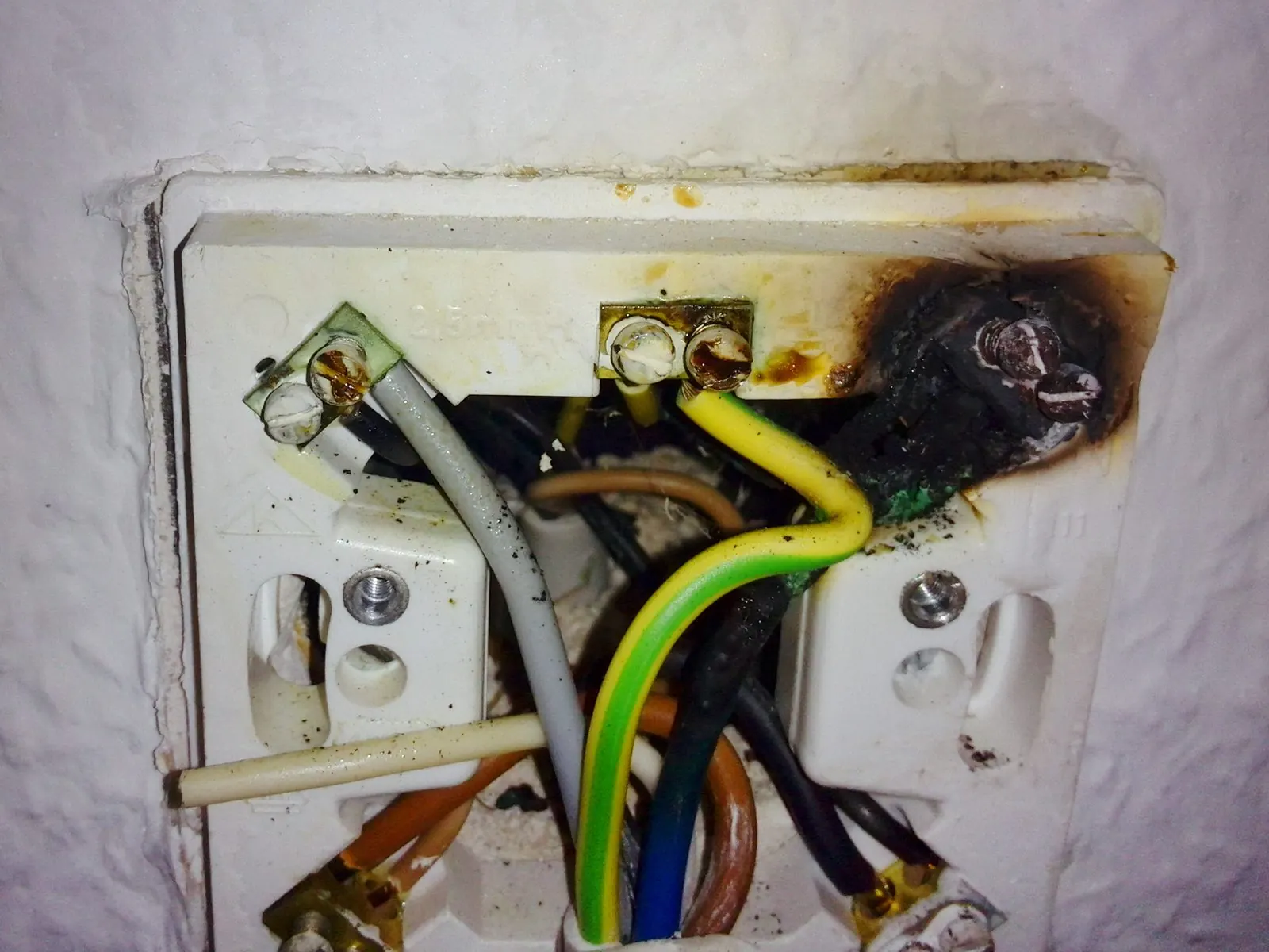 Caja de enchufe empotrada con los cables y el plástico ennegrecidos por un cortocircuito