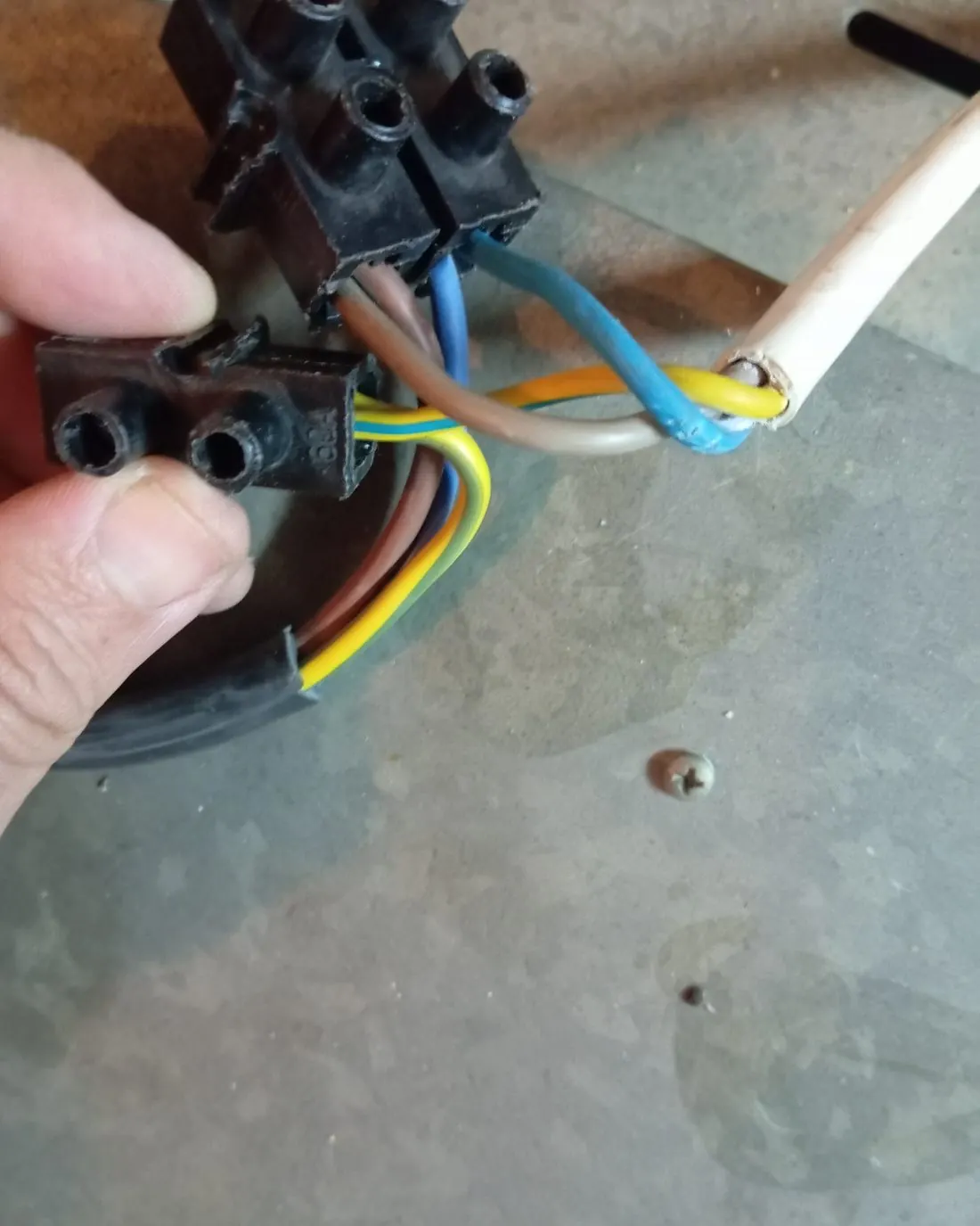 Mano sujetando una regleta de conexión con cables de colores pelados y empalmados