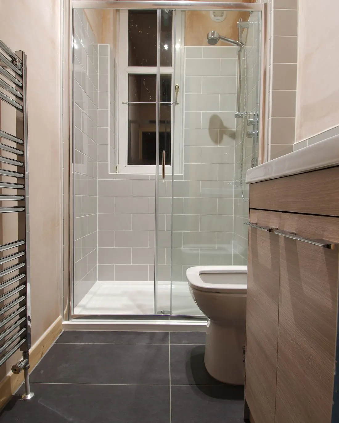 Baño reformado con plato de ducha y mampara, toallero radiador y mueble de lavabo