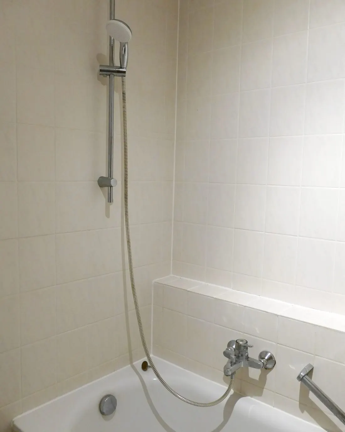 Bañera blanca con grifo termostático y barra de ducha en un baño alicatado