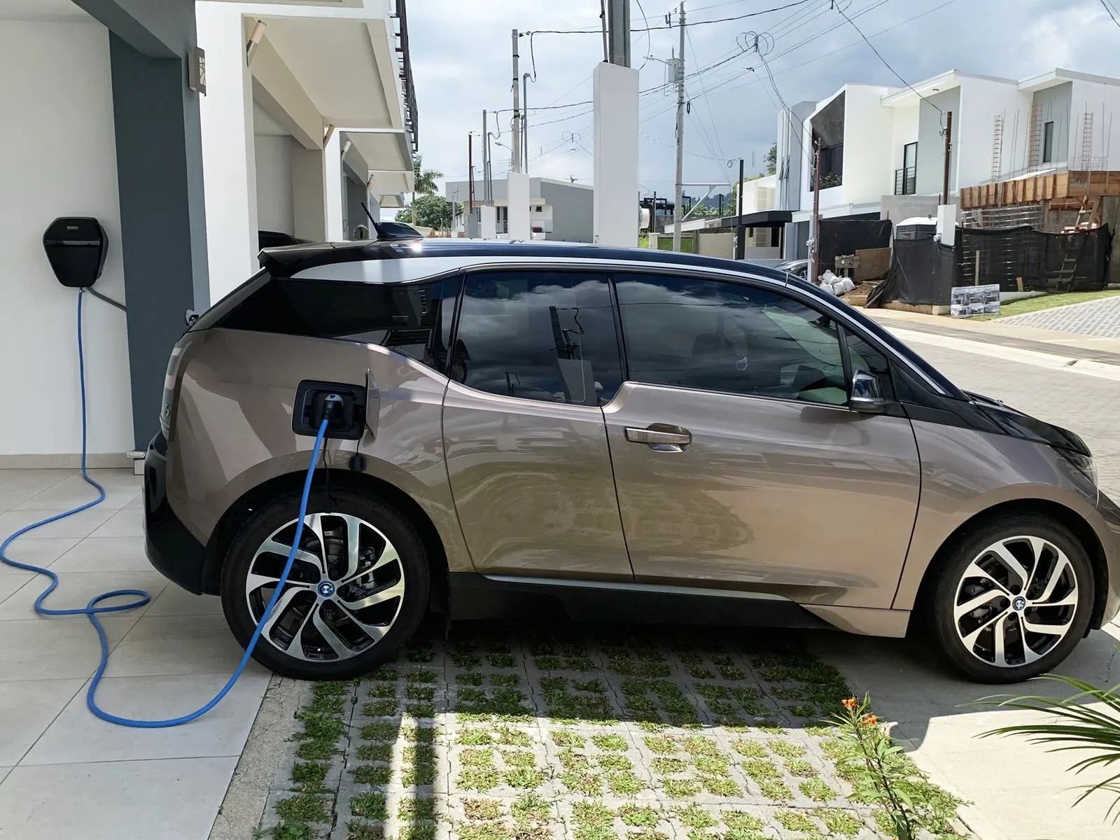 Coche eléctrico cargando en la entrada de una casa con el cable azul enchufado