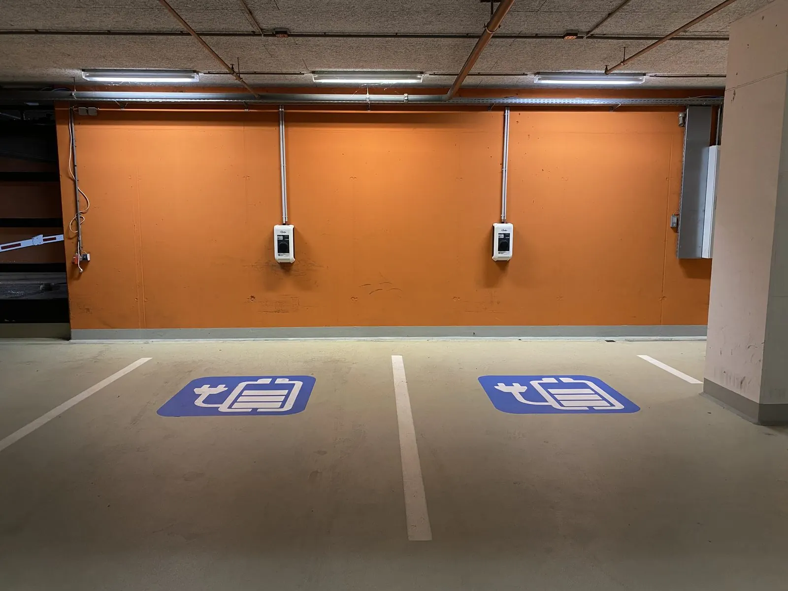 Dos cargadores de pared en plazas de garaje subterráneo señalizadas para coche eléctrico