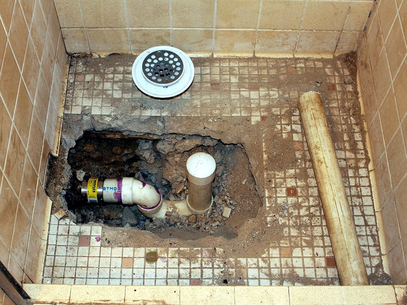 Plato de ducha levantado con el desagüe y la tubería al descubierto para repararlos