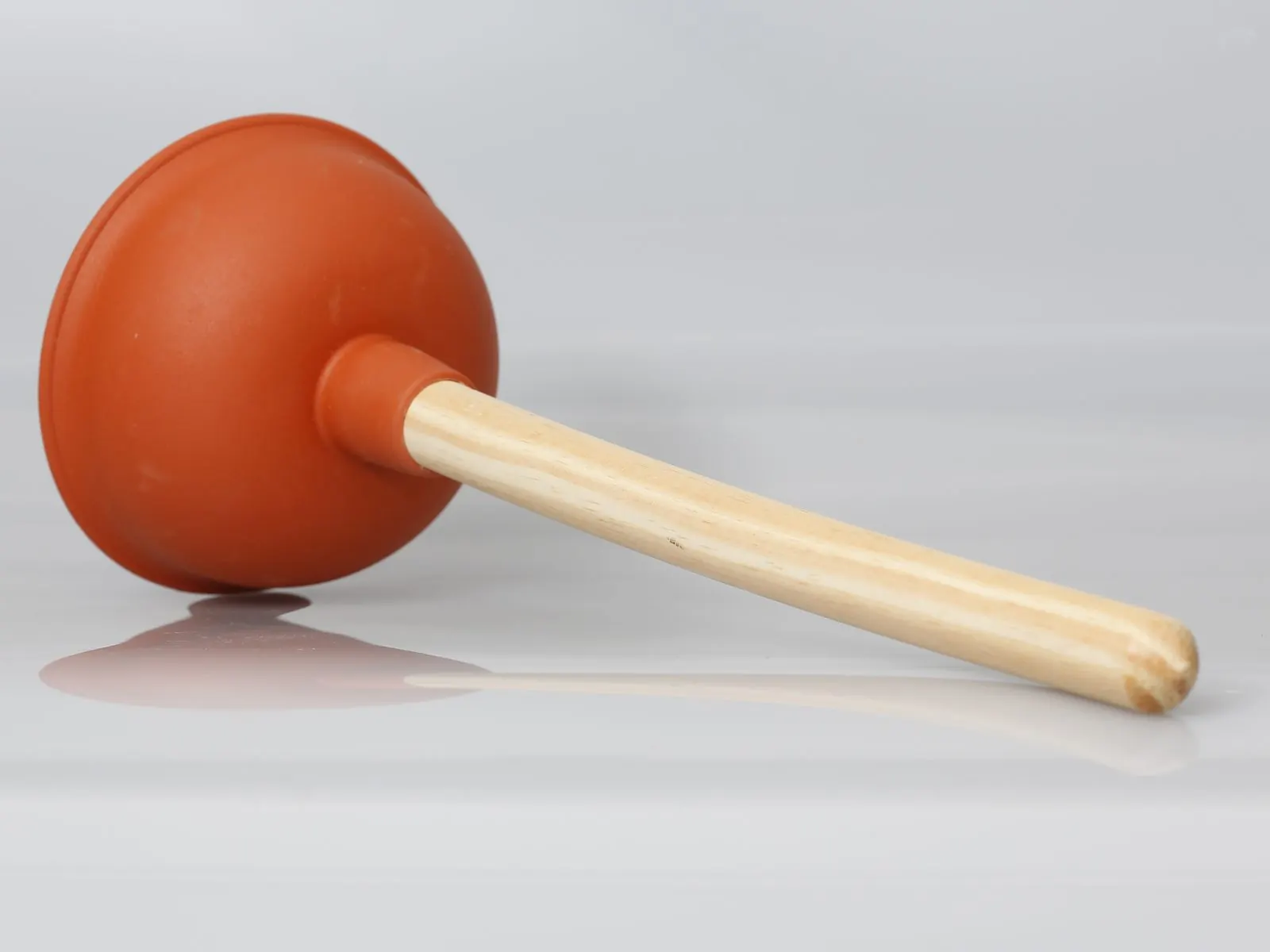 Desatascador de ventosa naranja con mango de madera sobre fondo blanco
