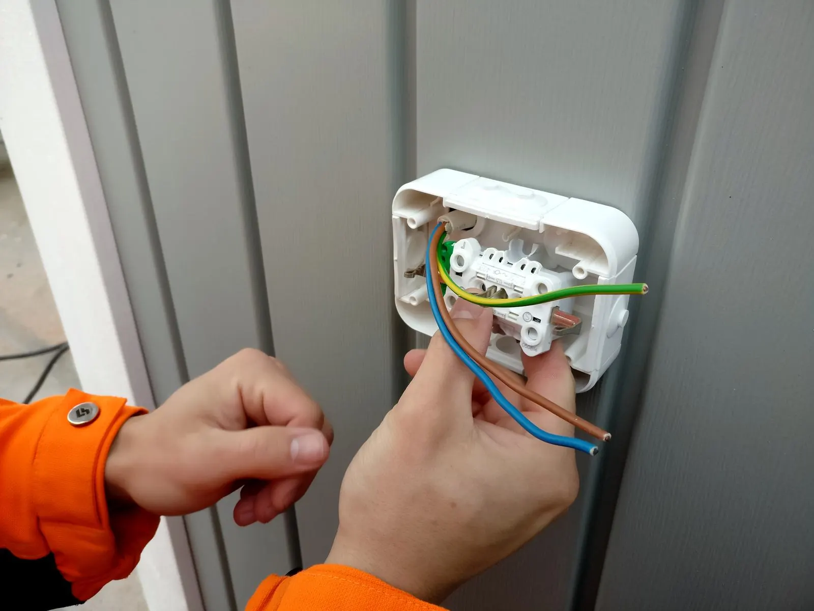 Manos conectando los cables de un enchufe de superficie atornillado a una pared gris