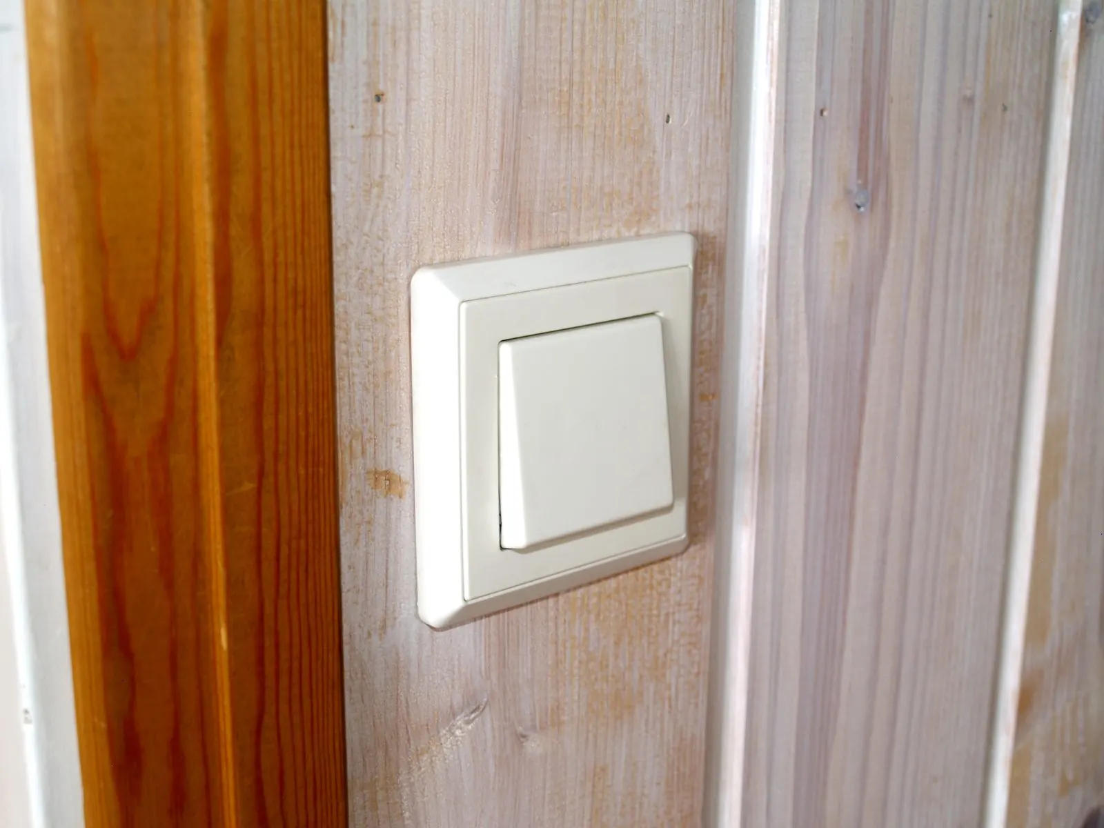 Interruptor de luz blanco de tecla ancha montado en una pared junto a un marco de madera