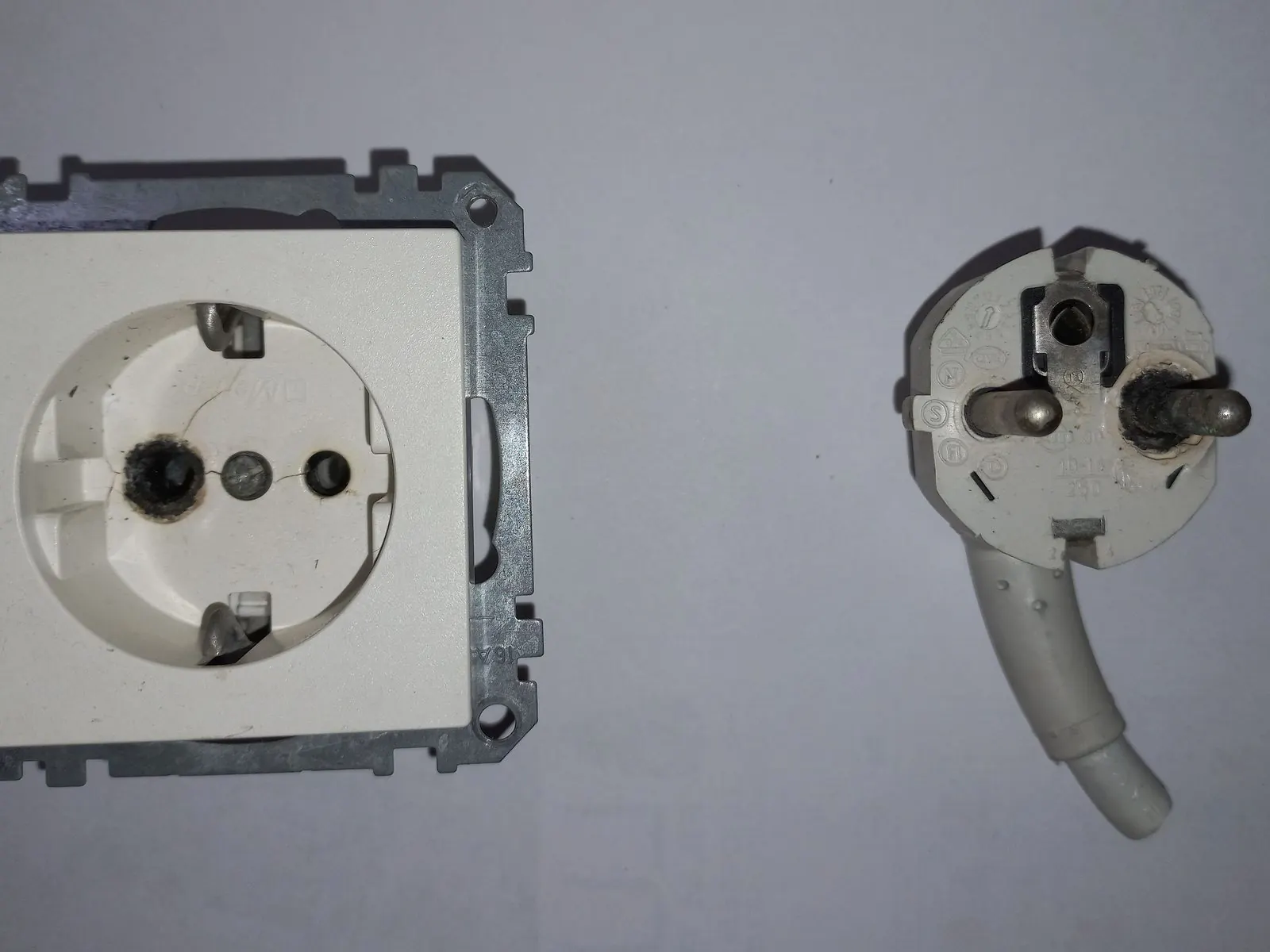 Base de enchufe Schuko empotrada en la pared y una clavija con toma de tierra al lado
