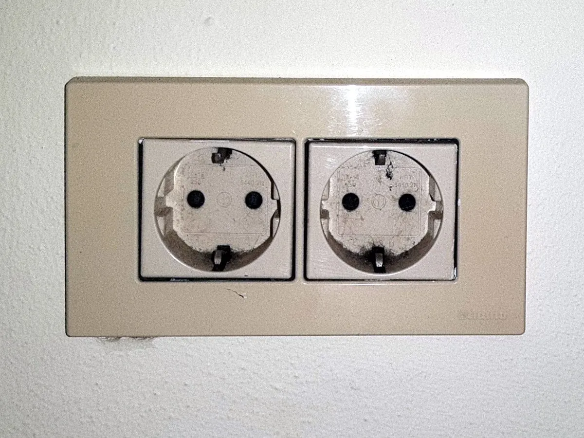 Enchufe doble Schuko con marco beige empotrado en una pared blanca