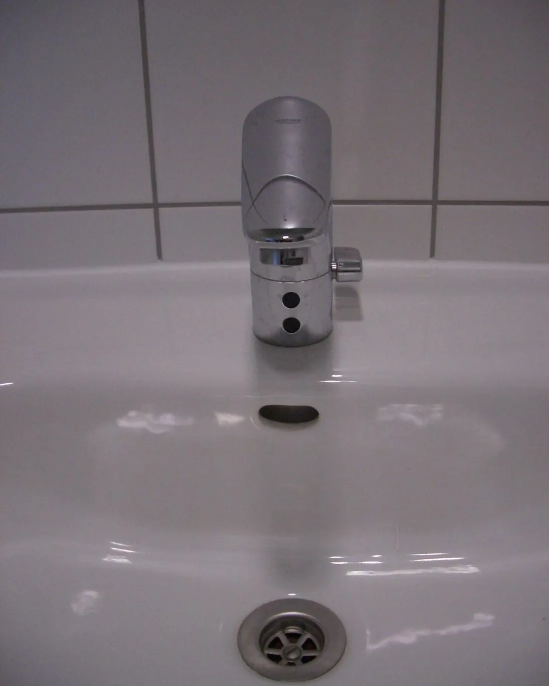Grifo de lavabo cromado con sensor de ahorro de agua en un baño alicatado