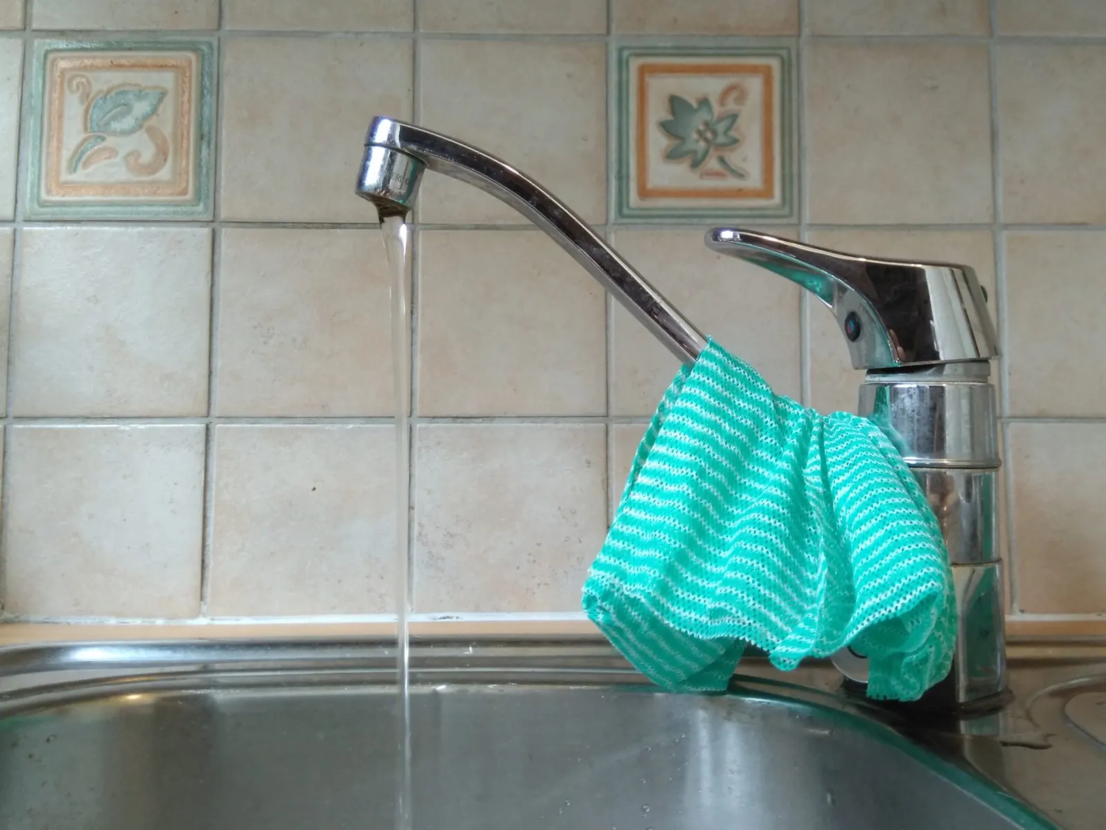 Grifo de cocina con caño alto echando agua y una bayeta colgada de la maneta