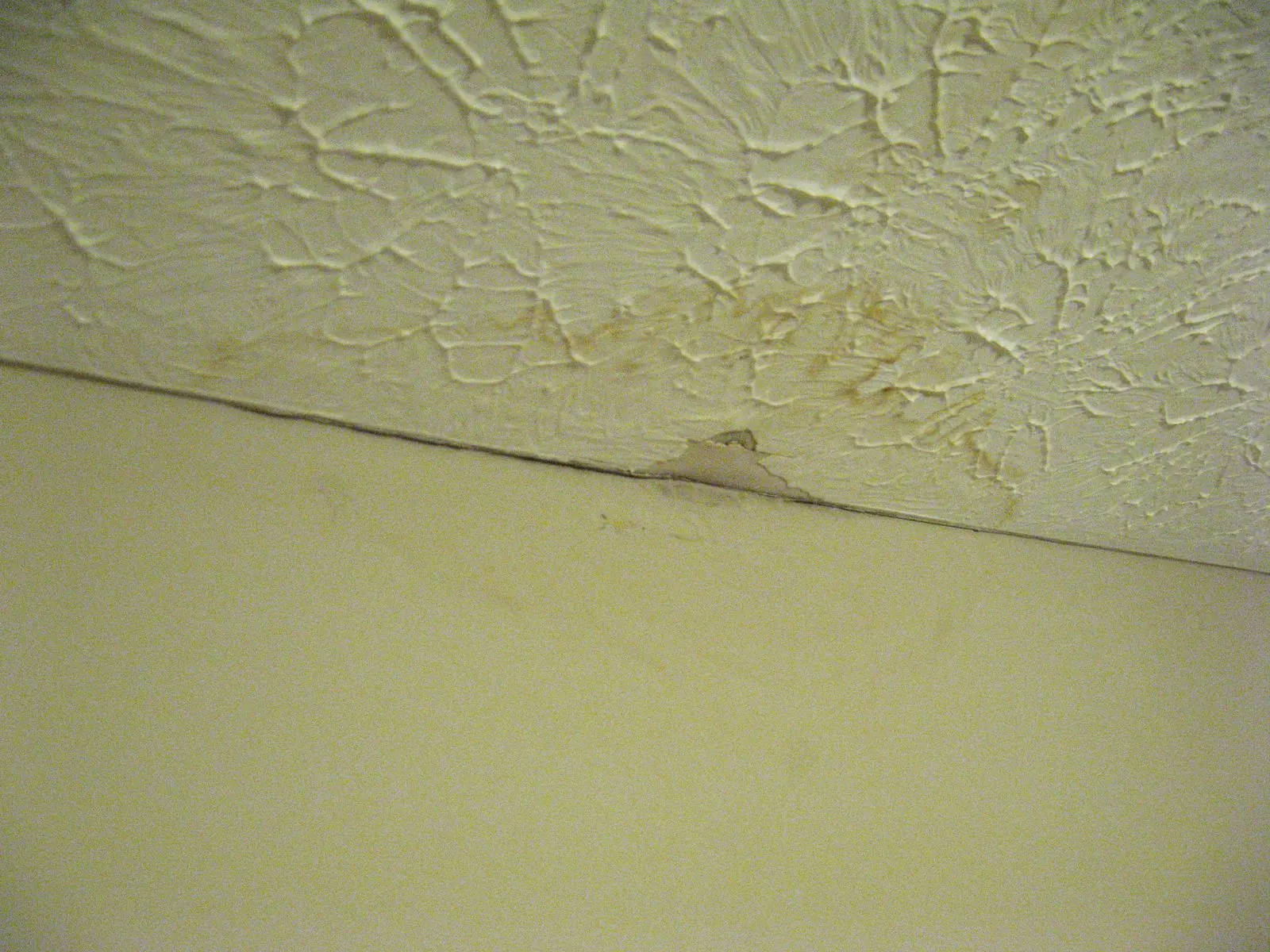 Mancha amarillenta de agua en el techo de gotelé junto a la unión con la pared