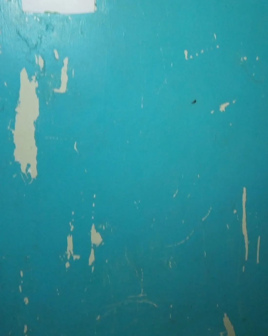 Pared pintada de azul turquesa con la pintura levantada en varias zonas por la humedad